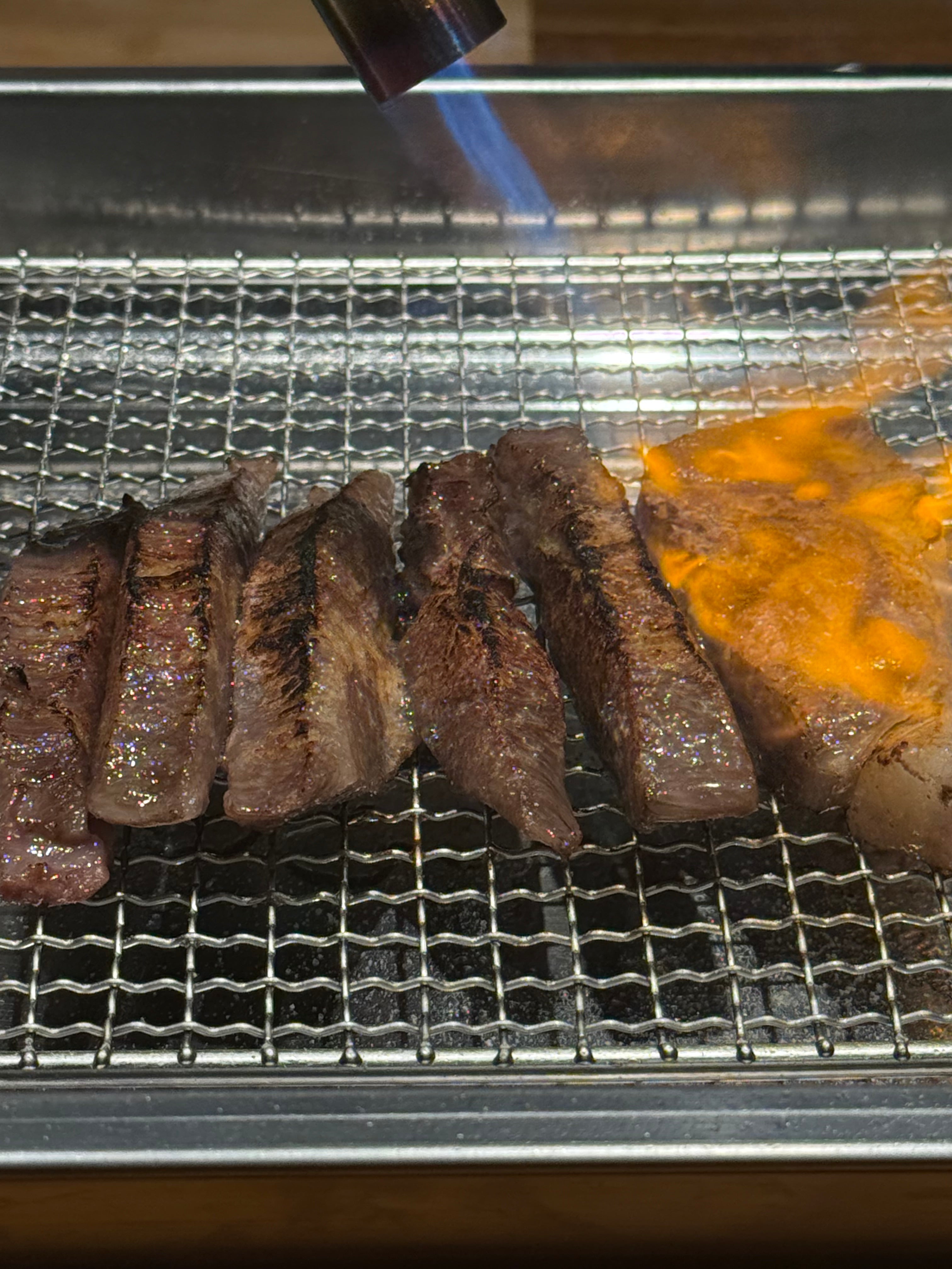 Marbled Wagyu strips seared on a grill with a blowtorch flame